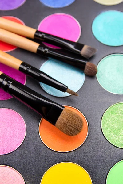 Make-up brushes and colorful eyeshadow palette over black — Stock Photo, Image