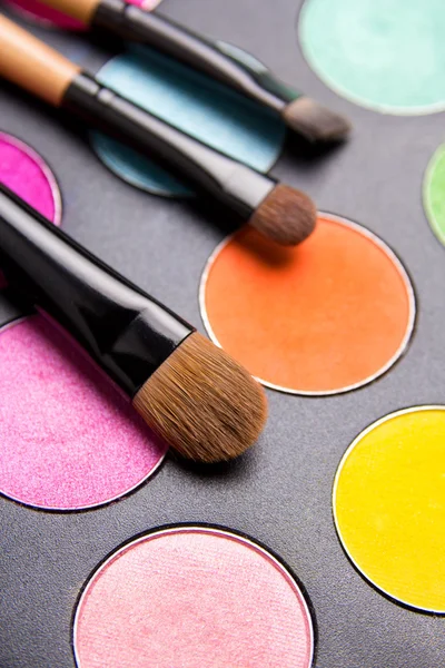 Make-up brushes and colorful eyeshadow palette over black close — Stock Photo, Image