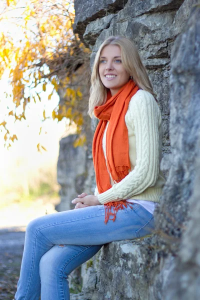 Молода красива жінка в теплому одязі, що сидить на кам'яній стіні — стокове фото