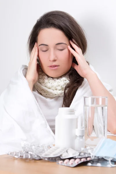 Ung kvinna med huvudvärk och bord med glas vatten och p-piller — Stockfoto