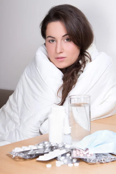 Jovem mulher ter gripe com pílulas sobre a mesa — Fotografia de Stock