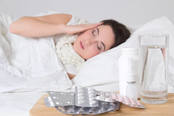 Chora kobieta w łóżku i tabletki na stole — Zdjęcie stockowe
