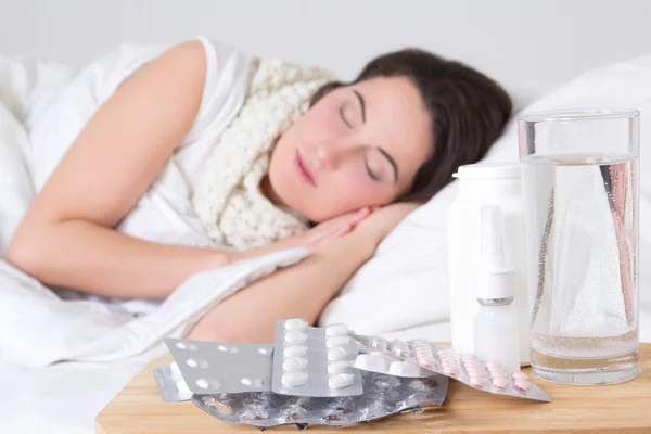 Joven mujer enferma durmiendo en la cama y las pastillas en la mesa — Foto de Stock