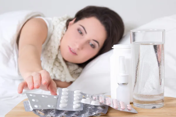 ベッドとベッドサイド テーブルの上の丸薬で病気の若い女性 — ストック写真