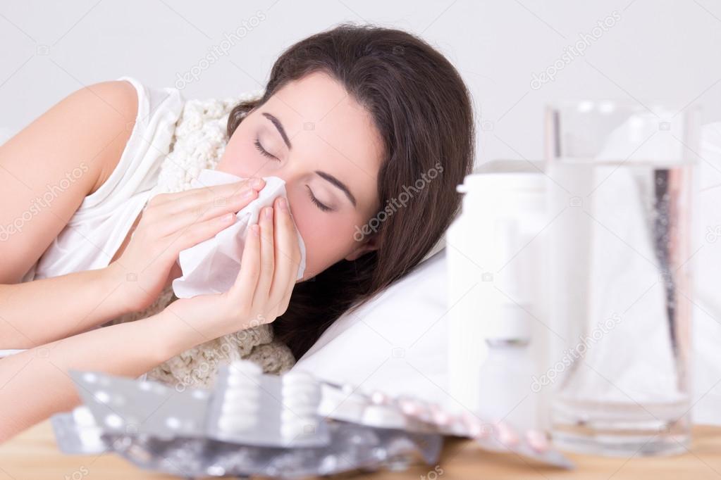 brunette woman sneezing in a tissue in the living room