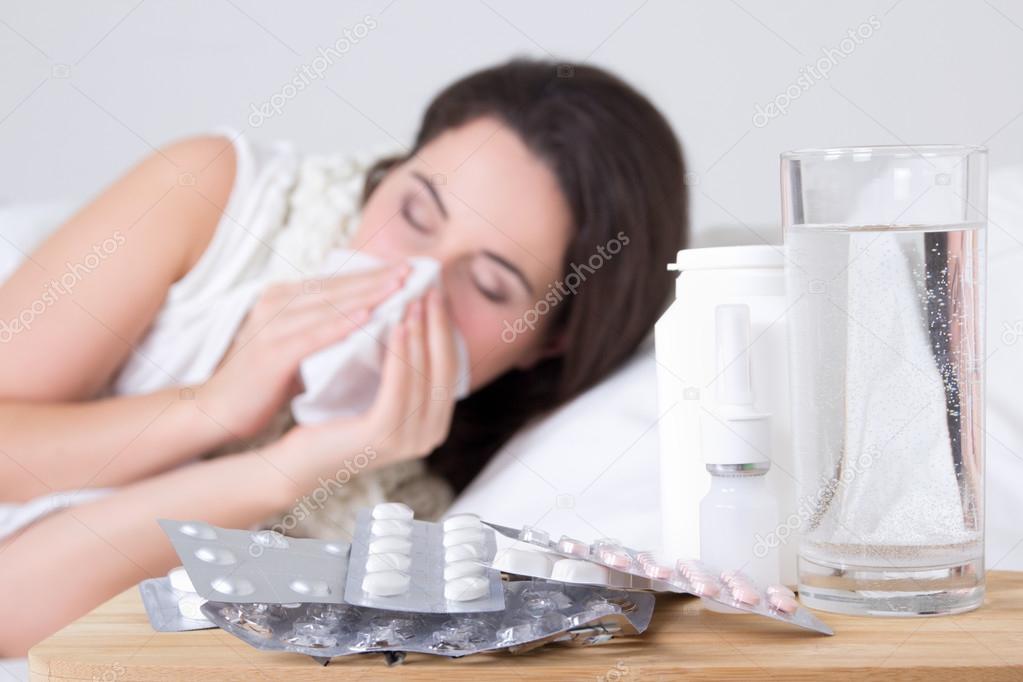 brunette woman sneezing in a tissue in the living room and pills