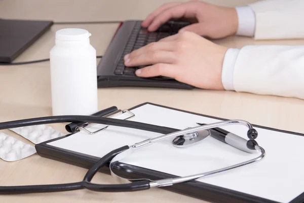 Estetoscopio, carpeta y las manos del doctor digitar en el teclado — Foto de Stock