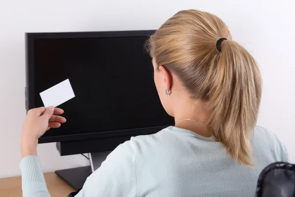 Back view of young woman holding visiting card and using pc — Stock Photo, Image