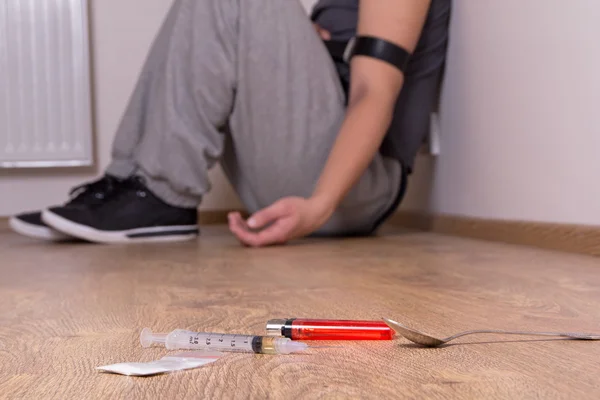 Syringe with drugs and addict sitting on the floor — Stock Photo, Image