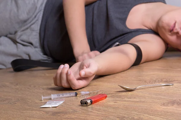 Шприц с наркотиками и наркоман, лежа на полу — стоковое фото