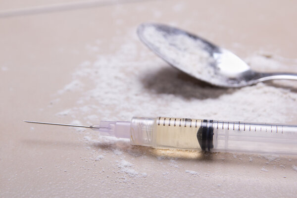 syringe with drug substance, heroin powder and spoon on the floo