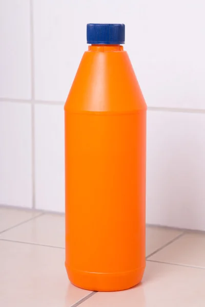 Orange plastic bottle of cleaning product on tiled floor — Stock Photo, Image