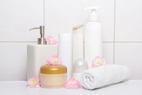 Set of white cosmetic bottles with flowers over tiled wall — Stock Photo, Image