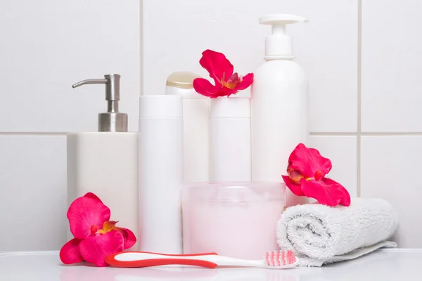 Sada bílých kosmetických lahví s červenými květy nad obkládačkách — Stock fotografie