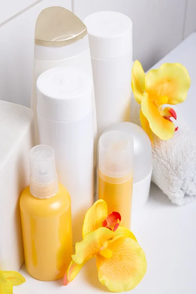 Group of cosmetic bottles with orange flowers over white tiled w — Stock Photo, Image