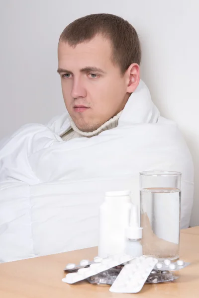 Sick man and table with glass of water and pills — Stock Photo, Image