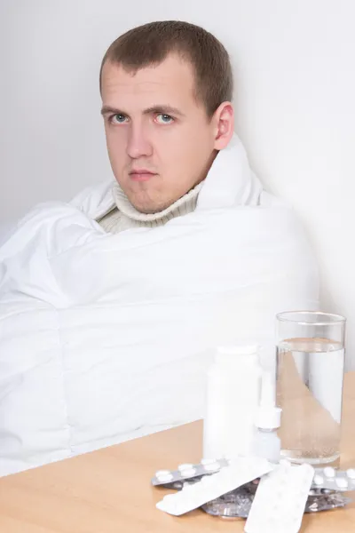 Enfermo sentado y mesa con vaso de agua y pastillas — Foto de Stock