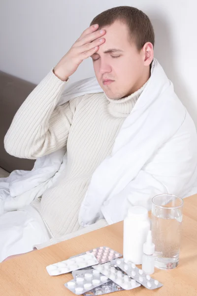 Молодой человек с головной болью и таблетки на столе — стоковое фото