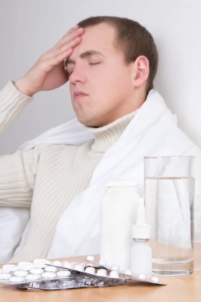 Junger Mann mit Kopfschmerzen und Pillen auf dem Tisch. Tabletten im Fokus — Stockfoto