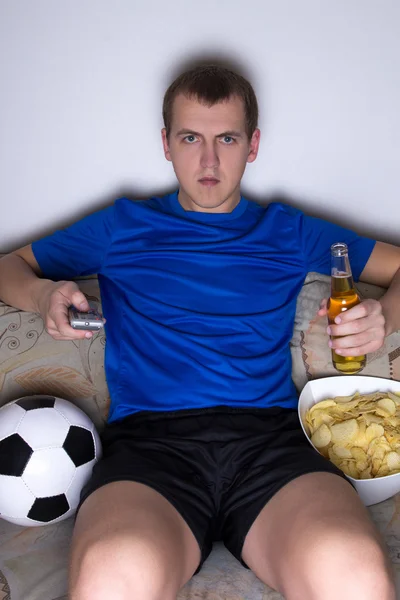 Hombre aburrido en el fútbol uniforme sentado en la sala de estar y ver —  Fotos de Stock