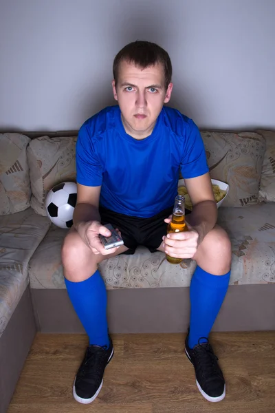Zwolennikiem jednolitego siedzi na kanapie i oglądanie piłki nożnej w — Zdjęcie stockowe