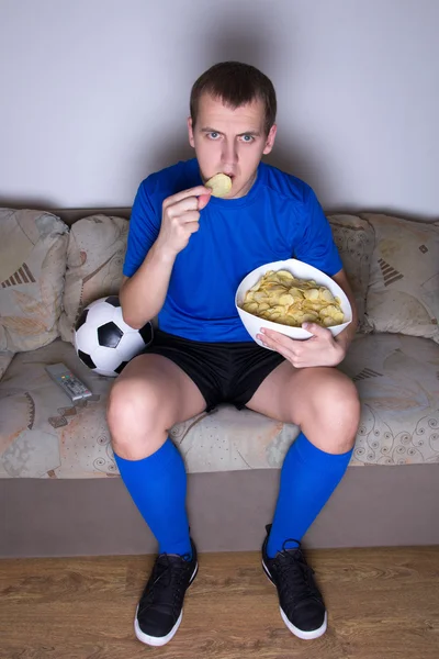 Partidario viendo el fútbol en la televisión en casa y comiendo patatas fritas —  Fotos de Stock