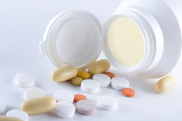 Close up of colorful pills pouring from plastic bottle over whit — Stock Photo, Image