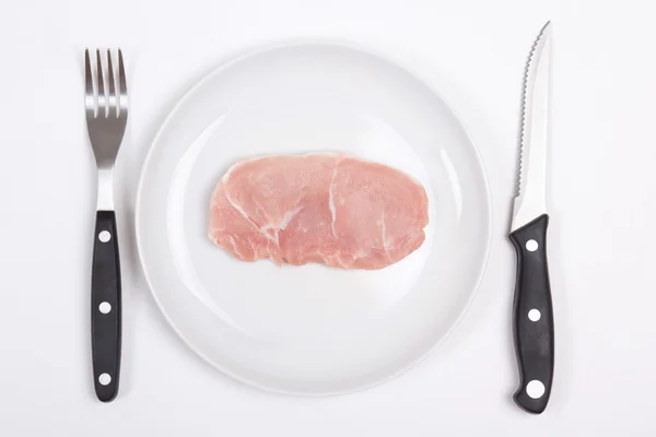 Chuleta de cerdo cruda fresca en un plato con tenedor y cuchillo — Foto de Stock