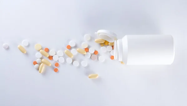 Pílulas coloridas derramando de garrafa de plástico sobre branco — Fotografia de Stock