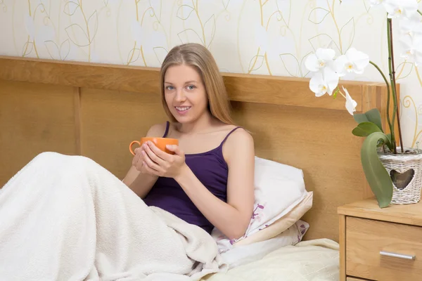 女人坐在床上用的早晨喝咖啡的杯子 — 图库照片