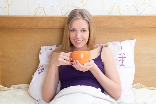 Atractiva mujer sentada en la cama con la taza de café o té —  Fotos de Stock