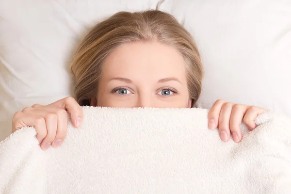 Happy young woman lying in bed under blanket — Stock Photo, Image