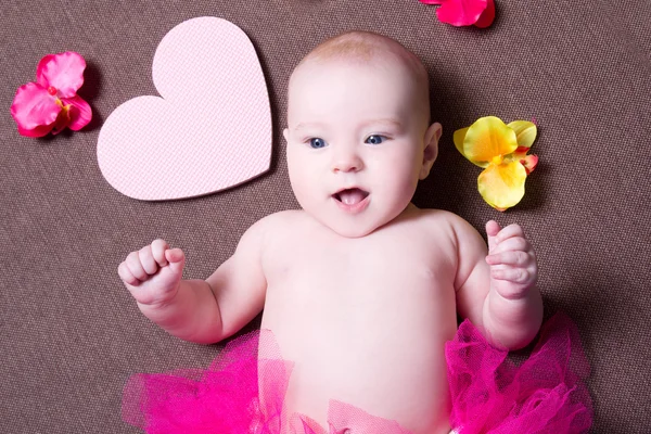 Portrait of beautiful baby girl in pink skirt lying with hearts — Stock Photo, Image