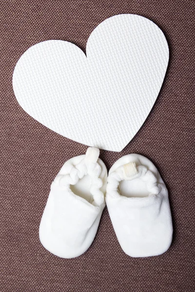 Zapatos de bebé y plástico corazón sobre marrón —  Fotos de Stock