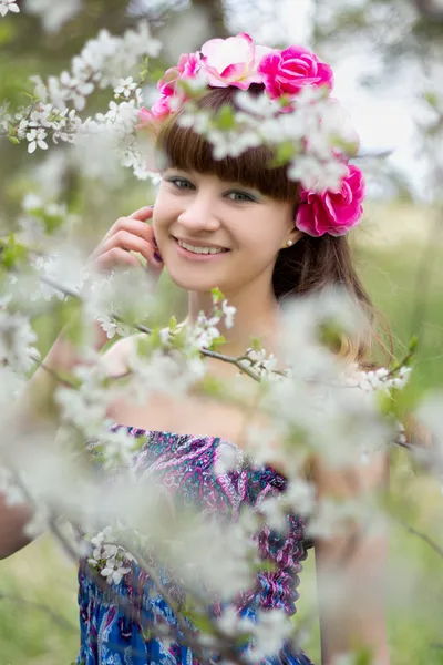 Lycklig tonåring med blommor på huvudet i trädgården — Stockfoto