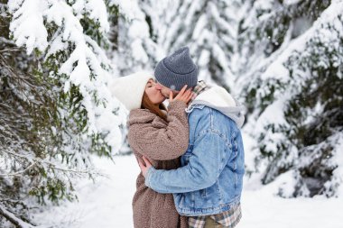 Genç adam ve kadın kış ormanında öpüşüyor.