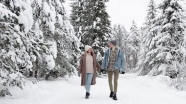 Mutlu genç çift kış ormanında yürüyor ve öpüşüyor.