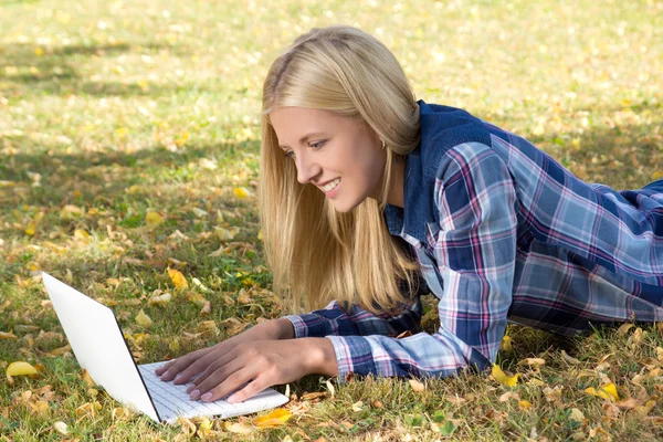 美丽的女人躺在片秋色的公园和使用便携式计算机 — 图库照片