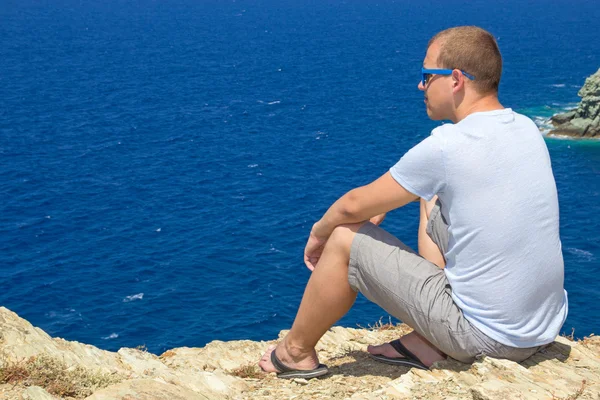 坐在海岸的岩石峭壁上的男人 — 图库照片