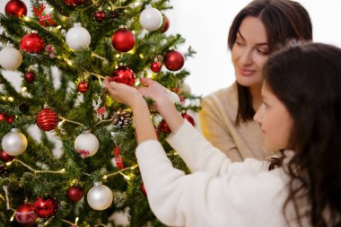 Noel gelenekleri. Mutlu bir kadın ve Noel ağacını süsleyen tatlı küçük kızının yakın çekimi.