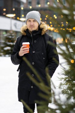 Noel pazarında elinde bir fincan kahveyle sokakta yürüyen bir adam.