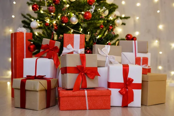 圣诞彩灯背景下灰色墙壁上装饰过的圣诞树下堆放的礼品盒 — 图库照片