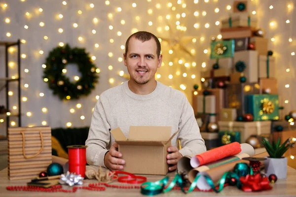 긍정적 남자가 식탁에 크리스마스 선물을 포장한다 — 스톡 사진