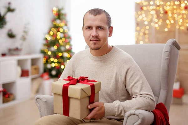 ハンサムな男とともにギフト座っているアームチェアでクリスマスインテリア — ストック写真