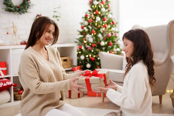 크리스마스 아름다운 어머니가 크리스마스 트리로 장식된 거실에서 딸에게 크리스마스 선물을 — 스톡 사진