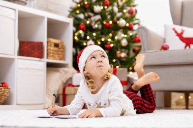 Hoş bir kız Noel Baba 'ya dekore edilmiş oturma odasında mektup yazıyor.