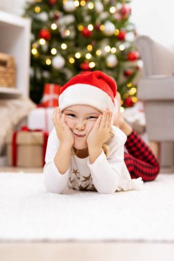 Evdeki Noel ağacının yanındaki halıya uzanmış komik küçük kız.