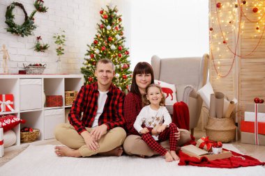 Pijamalı mutlu bir aile Noel ağacının yanında oturuyor.