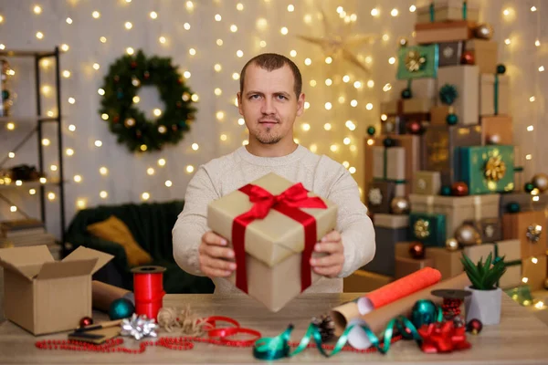 ハンサムな男が家に座って赤い弓で贈り物を示す — ストック写真