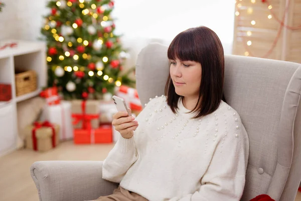 Ung Kvinna Med Telefon Sitter Fåtölj Jul Interiör — Stockfoto